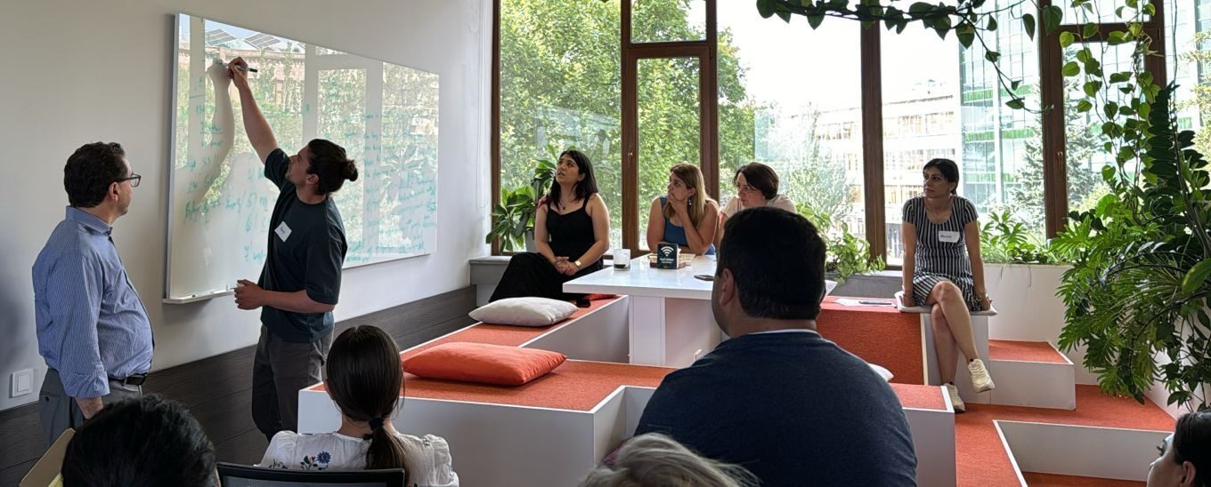 Group of people participating in a workshop in a modern room with big glass windows and large whiteboard and orange sofas