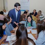 Man in blue suit standing with students seated at tables with papers