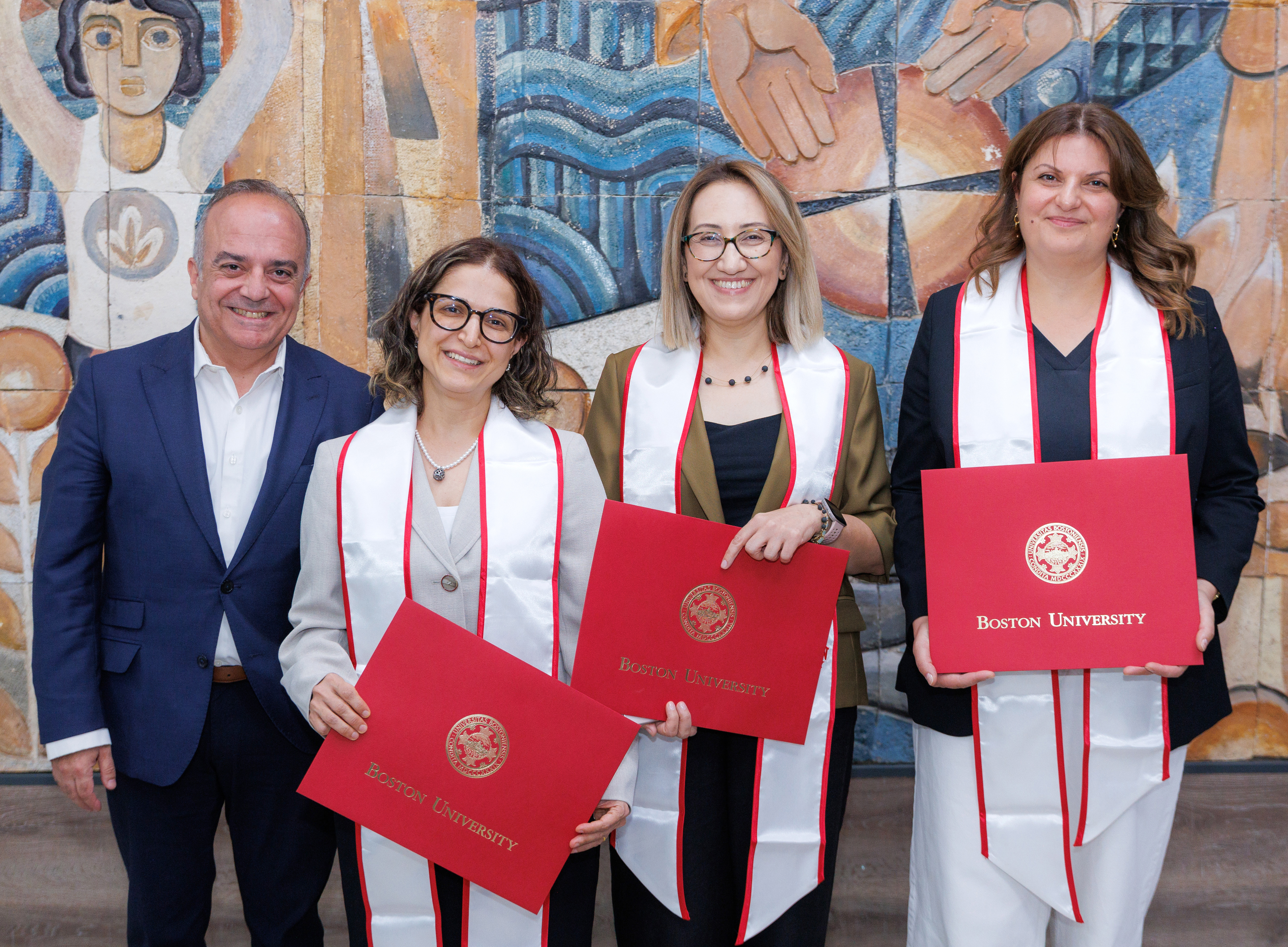 Three women holding BU diploma envelopes standing next to one man