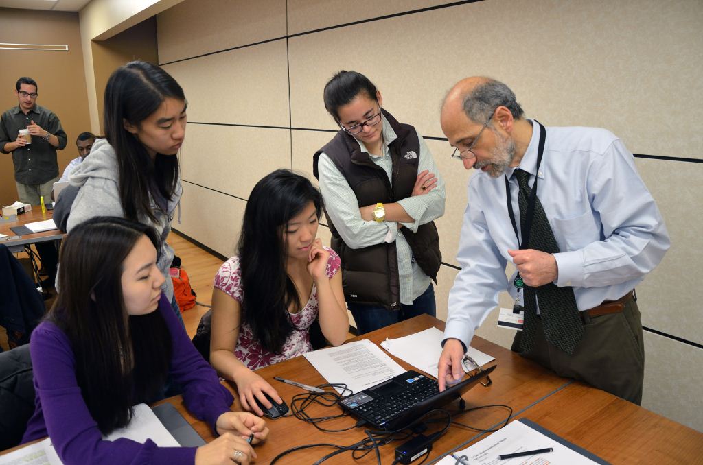 People gathered around a table, engaged in a discussion or collaborative activity, with papers and a laptop.