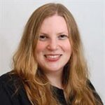 Head and shoulders of woman with long red/blond hair wearing dark top smiling