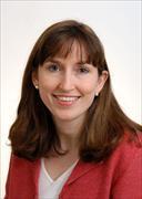 head and shoulders of woman smiling with straight dark brown hair to shoulders with bangs, small pearl earring studs, red suit jacket and cream color v-neck shirt