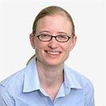 Woman with light brown hair pulled away from her face, dark framed eye glasses, light blue shirt smiling 