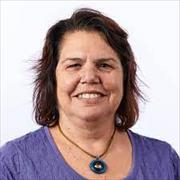 Head and shoulders shot of woman with chin length brown hair smiling broadly wearing purple shirt and necklace