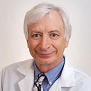 head and shoulders of light skin, white hair man wearing white lab coat blue shirt, patterned necktie slightly smiling into camera