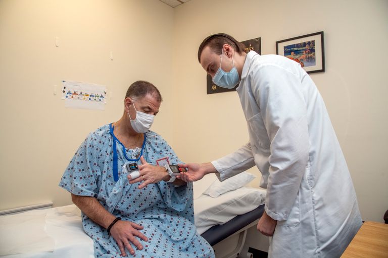Healthcare professional using a pulse oximeter on a patient's hand in a clinical setting.