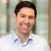 Man with very dark short hair, smiling broadly wearing white button down shirt open at neck