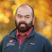 head and shoulders of Jon Wisco wearing dark BU logo jacket, red shirt, dark facial hair smiling with fall leaves in background