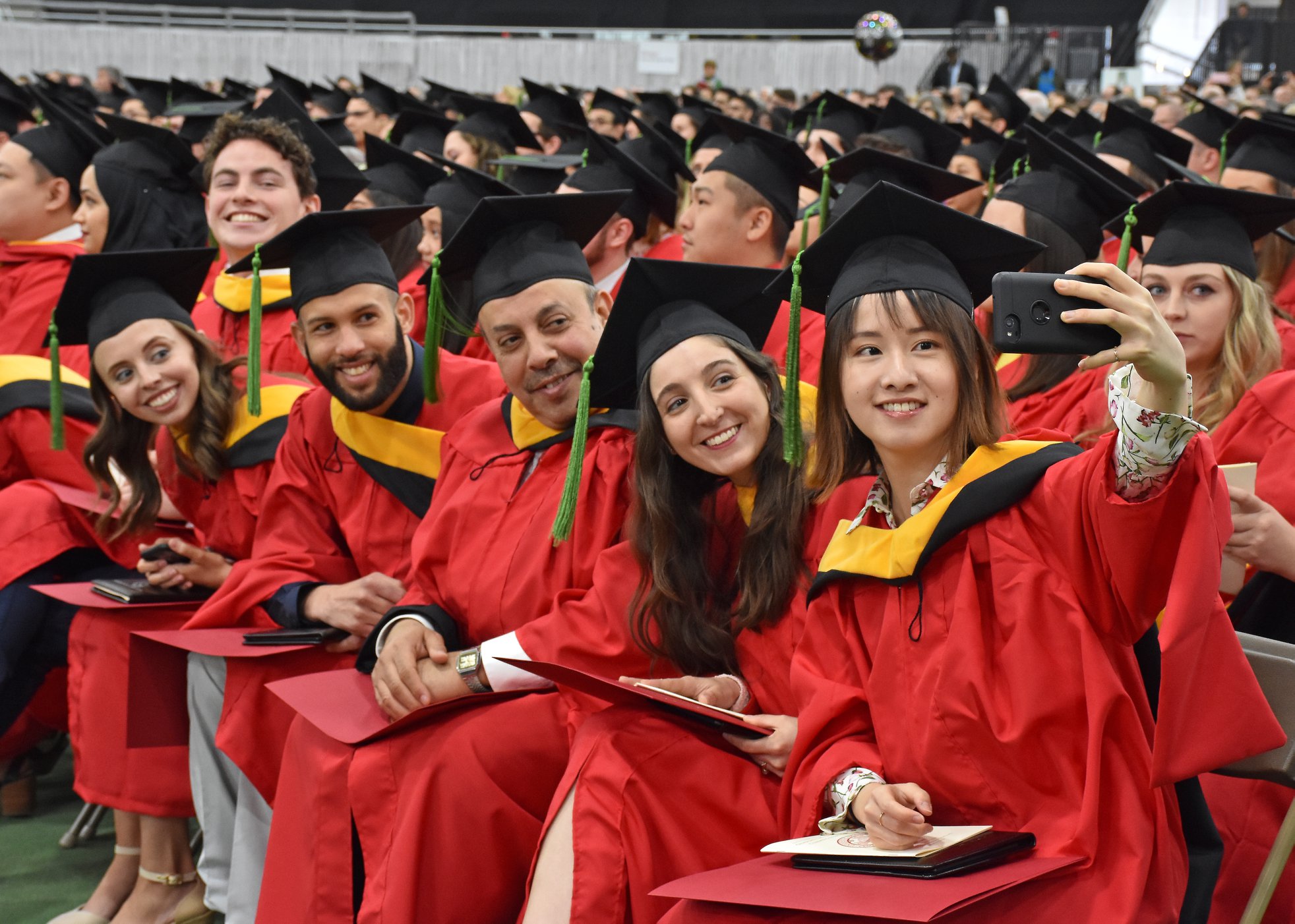Students in red gowns and gold and black hood taking a picture at convocation.