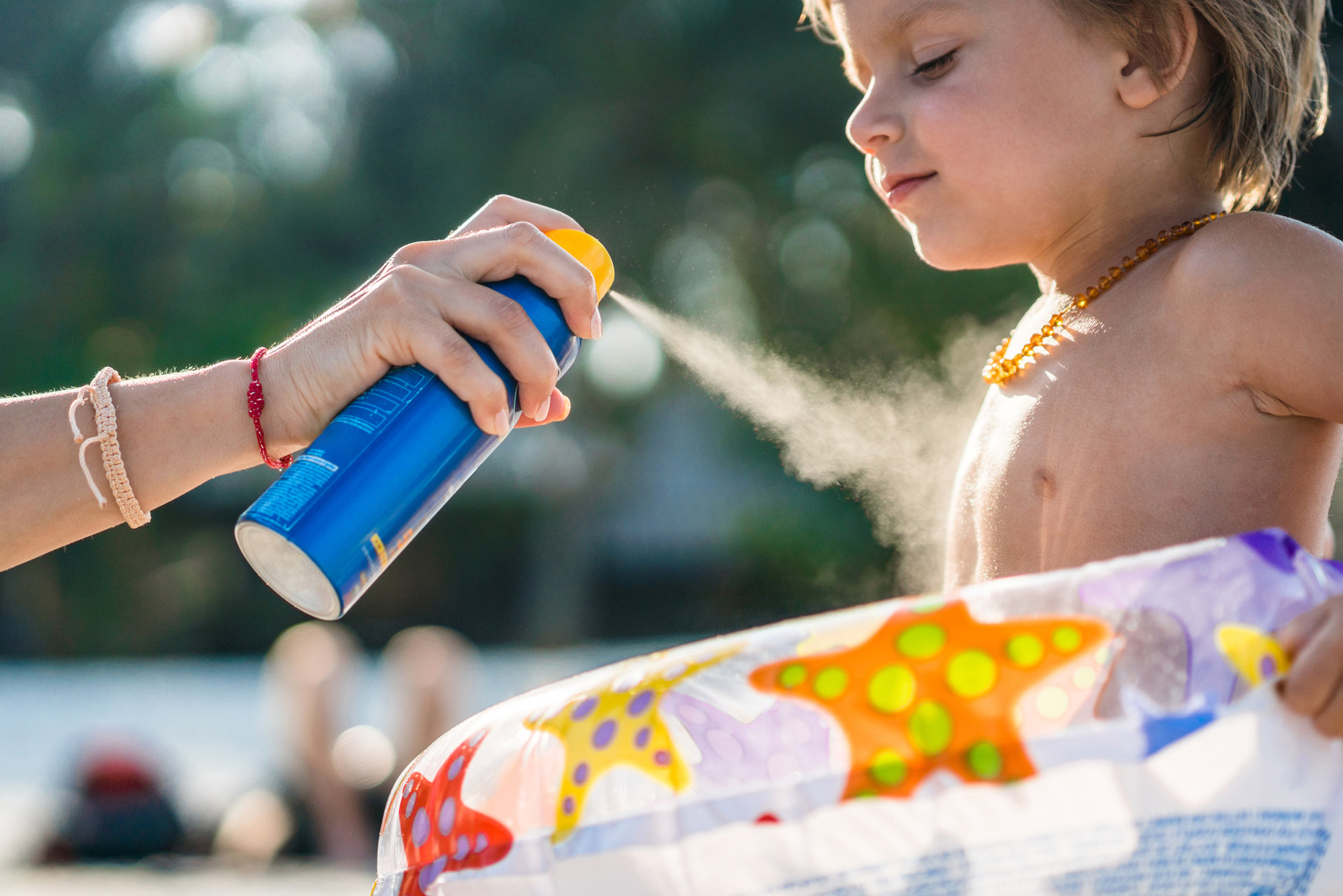 Female hand spraying sunscreen out of an aerosol can on a toddler 