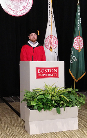 Stephen Wright in red robe behind white podium giving commencement speech