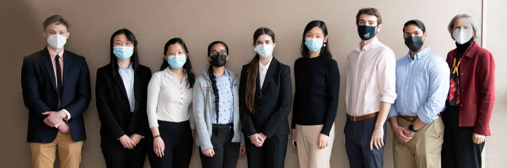 Eight Serchuk award winners and Dean Antman masked standing against a beige wall