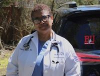 Dr. Chapman in her whitecoat outside leaning against a car with a BU sticker in red