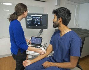 Two medical students use ultrasound machine on forearm and view image on screen.