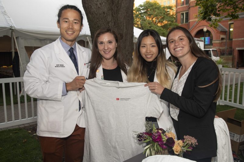 Four medical students display a t-shirt with the new name of the School of Medicine