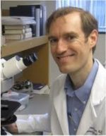 Headshot of Dr. Wilson in a whitecoat next to a microscope.