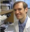 Headshot of Dr. Wilson in a whitecoat next to a microscope.