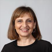 head and shoulders image of Venetia Zachariou wearing a black round neck top, shoulder length light brown hair smiling broadly