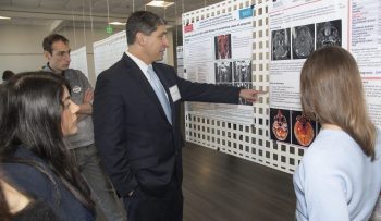 Two students with faculty member who is pointing at poster