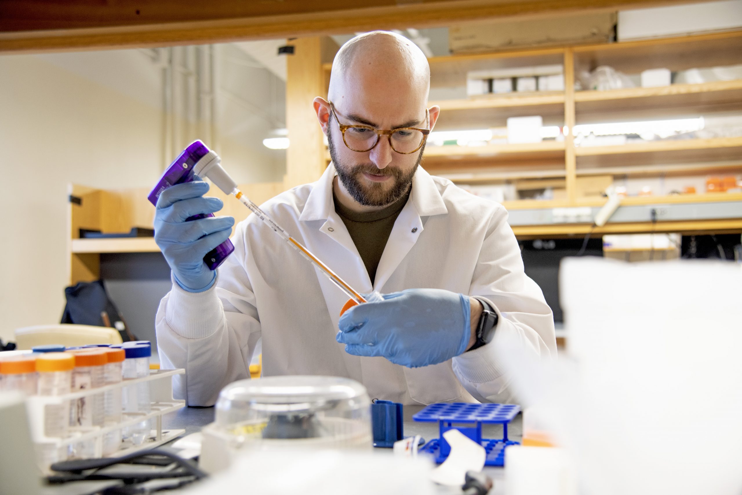 Marc Vittoria wearing a white labcoat and blue gloves working in the lab