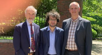 Drs. Samet, Nadareishvili and Lunze stand outdoors infront of a brick wall, BMC sign with green grass and trees