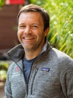 Head and shoulders shot of Michael Wallace casually dressed in gray patagonia fleece jacket, blue t-shirt. he has dark hair and beard, smiling broadly into camera