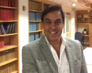head and shoulders of Noyan Gokce wearing white shirt, gray suit jacket in front of wooden bookcases, smiling