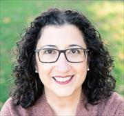 Headshot of Katharine O'Connell White, dark shoulder length curly dark brown hair, fair complexion, dark eye glasses smiling into camera