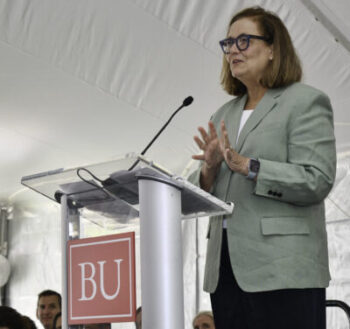 Kate Walsh standing behind podium labeled BU under white tent on whitecoat day
