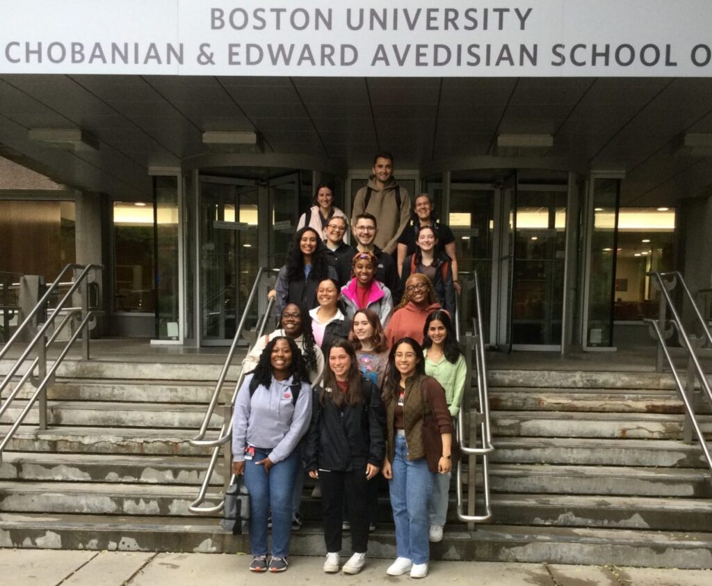 Participants standing on front steps of Chobanian Avedisian School of Medicine Instructional Building. School sign above their heads