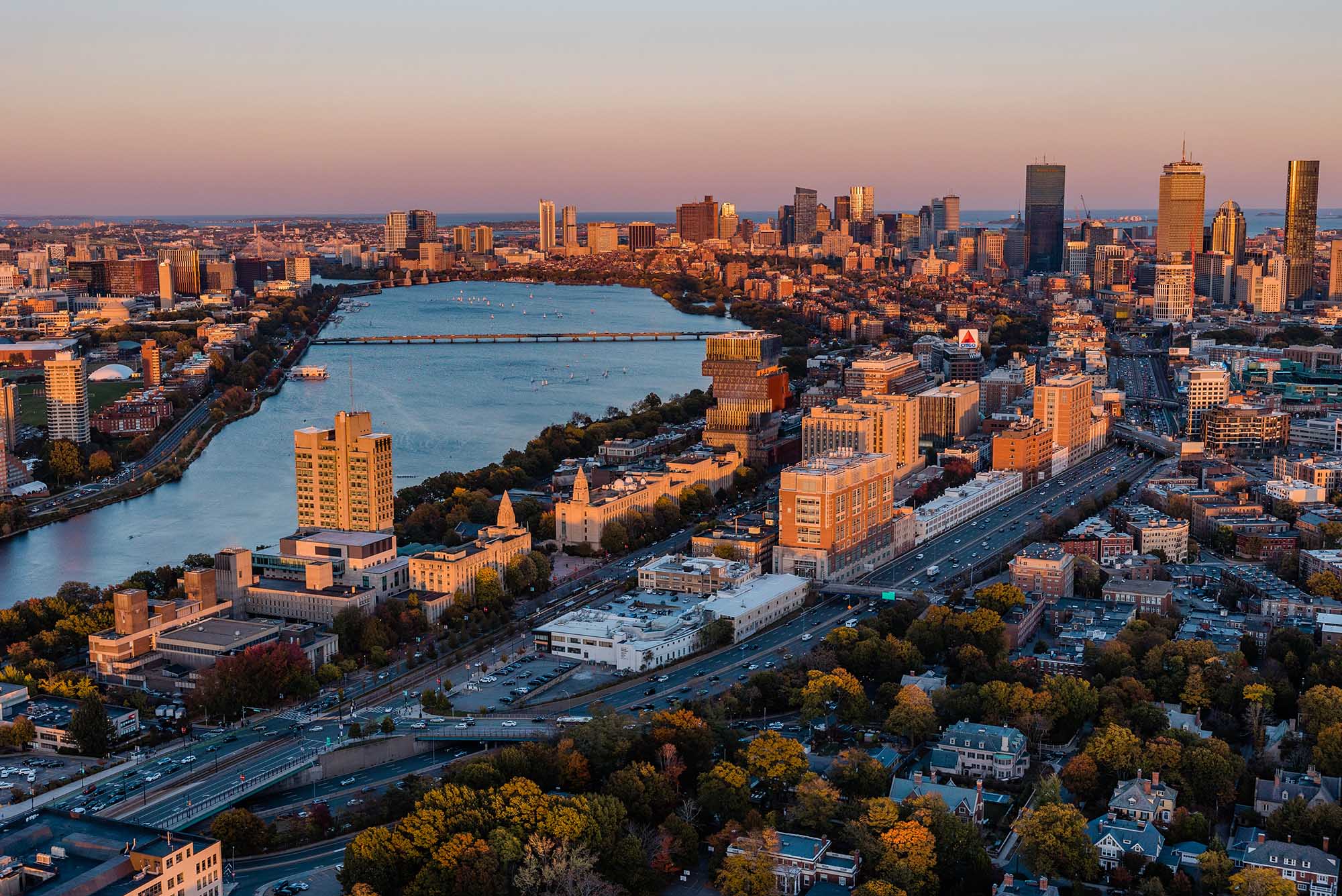 Aerial shot of Boston University's campus during sunset. An orange glow is shown on the large campus highlighting campus buildings like Kilachand.