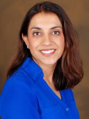 woman with shoulder length straight brown hair wearing blue long sleeved shirt, smiling