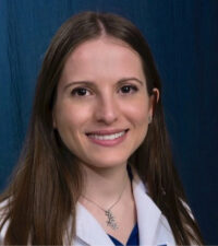 Head and shoulders of woman with light brown hair length beyond shoulders, white medical coat smiling broadly