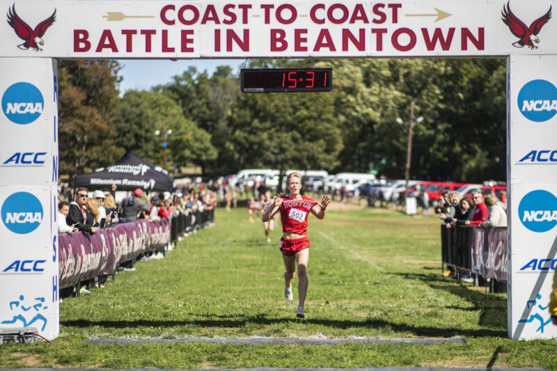 Man wearing red BU bib running in green path surrounded by spectators