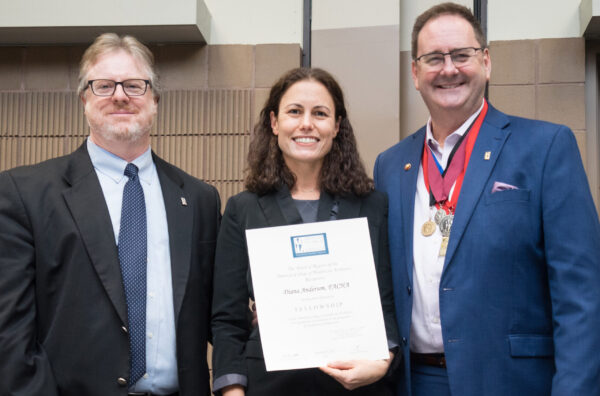 A woman holding a paper award smiling broadly with a man on each side of her