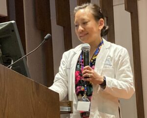 Woman wearing whitecoat standing at podium holding microphone