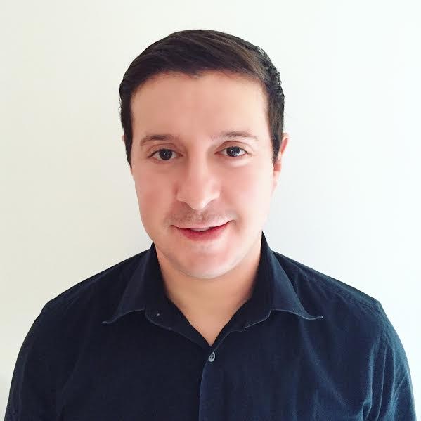 Image of man against plain white background with short dark hair, dark button up shirt, smiling.