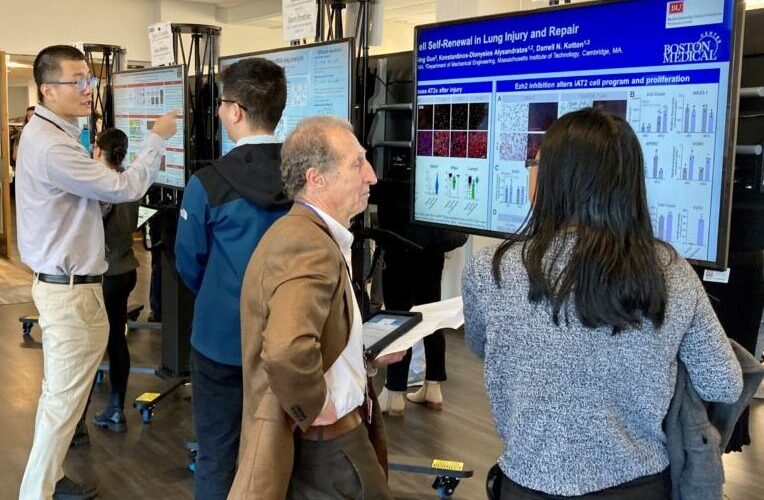 Four people talk in front of two large research posters