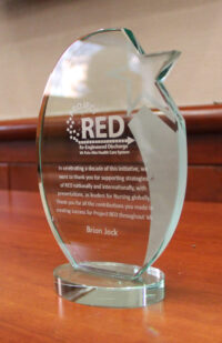 Irregularly shaped clear crystal award with writing etched on it, placed on a wood table