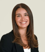 Woman with long brown hair past shoulders wearing dark jacket and white top, smiling broadly