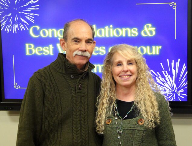 Man and woman smiling broadly in front of Congratulations and Best Wishes on your retirement banner in background