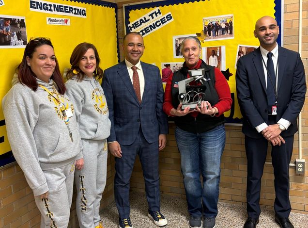 Five people gathered in front of yellow bulletin boards, Valeda Britton holding a microscope