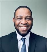 Head and shoulders shot of Temitope Ogundare wearing dark suit, white shirt blue/gray tie, smiling broadly