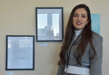 Woman standing next to two framed poems hanging beside her on a wall
