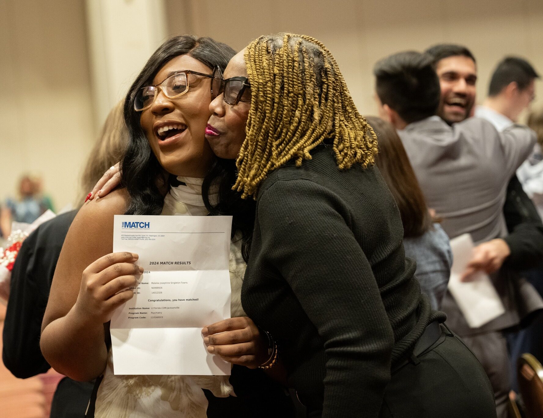 Foreground two women embracing one holding a match letter, background to men embracing holding a match letter