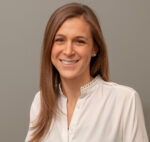 Head and shoulders shot of Katy Bockstall, straight hair light brown hair past shoulders, wearing white shirt, smiling broadly