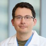 Head and shoulders of Dane Scantling wearing white coat, short brown hair, eyeglasses, gentle smile