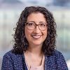 Head and shoulders of Katharine White, blue shirt, shoulder length brown curly hair, eyeglasses, smiling broadly