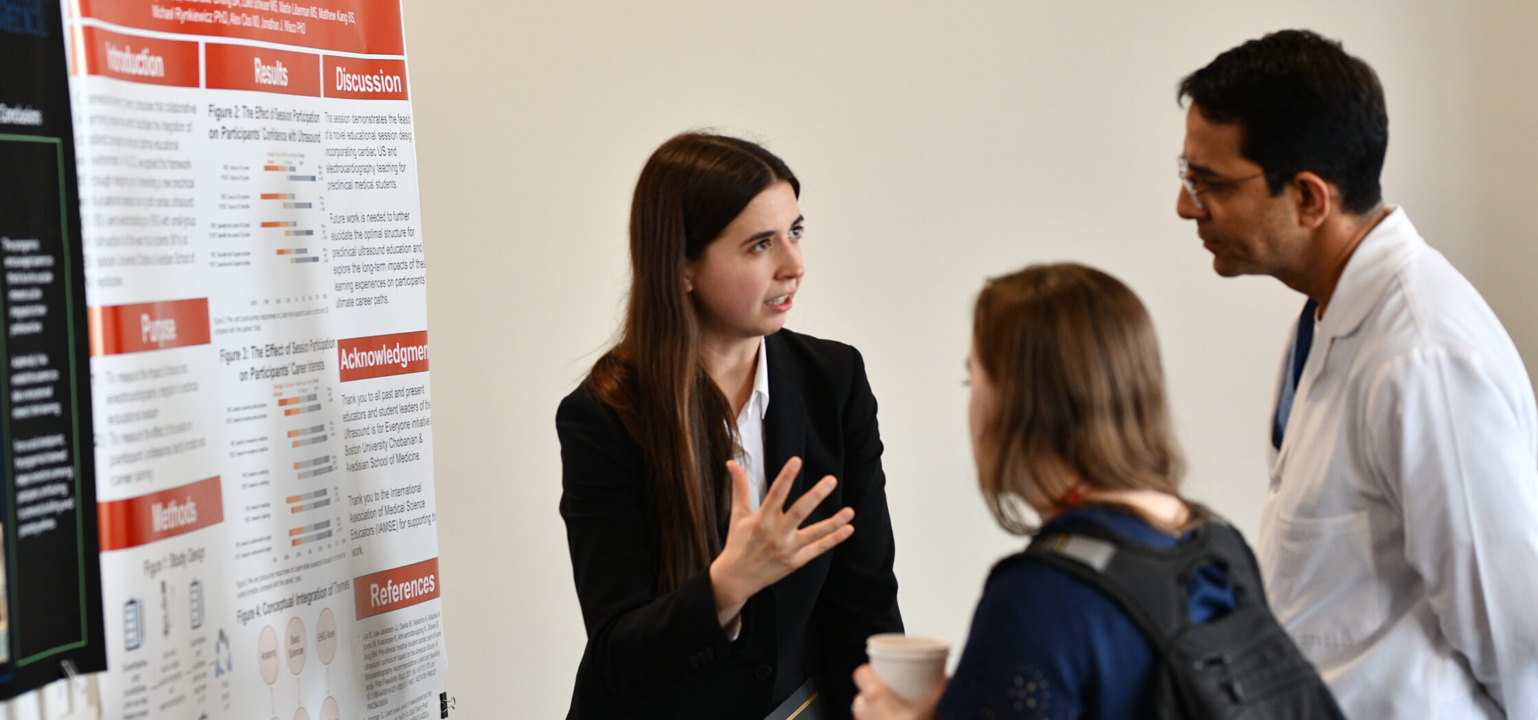 Three people talking in front of a poster hanging from ceiling