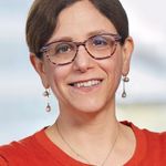 Head and shoulders of Dr. Bair-Merritt wearing red top, pearl earrings, brown eyeglasses, dark brown hair, smiling